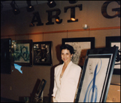Artist Brenda Heim standing with her art at a college exhibition of her work.
