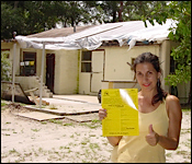 Artist Brenda Heim standing in front of her under construction studio holding a building permit with a thumbs up.